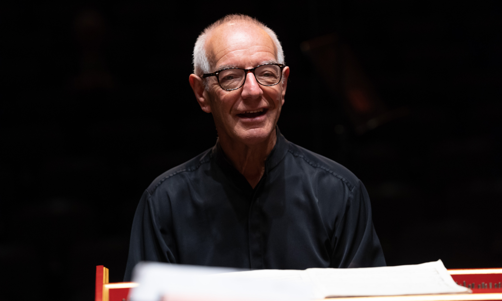 Principal Guest Conductor Nicholas Kraemer smiles while seated in front of a harpsichord.