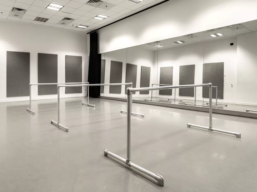Image of an empty rehearsal room filled with wall mirrors and three bars for dancers. 