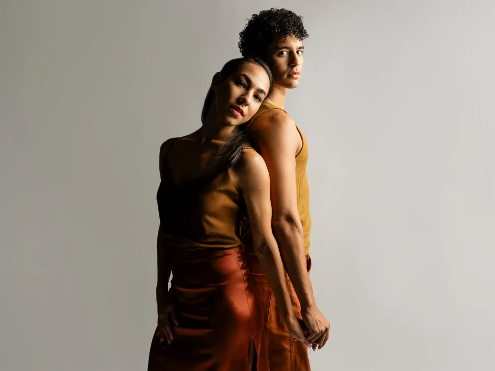 A man and woman stand back-to-back while holding hands. 