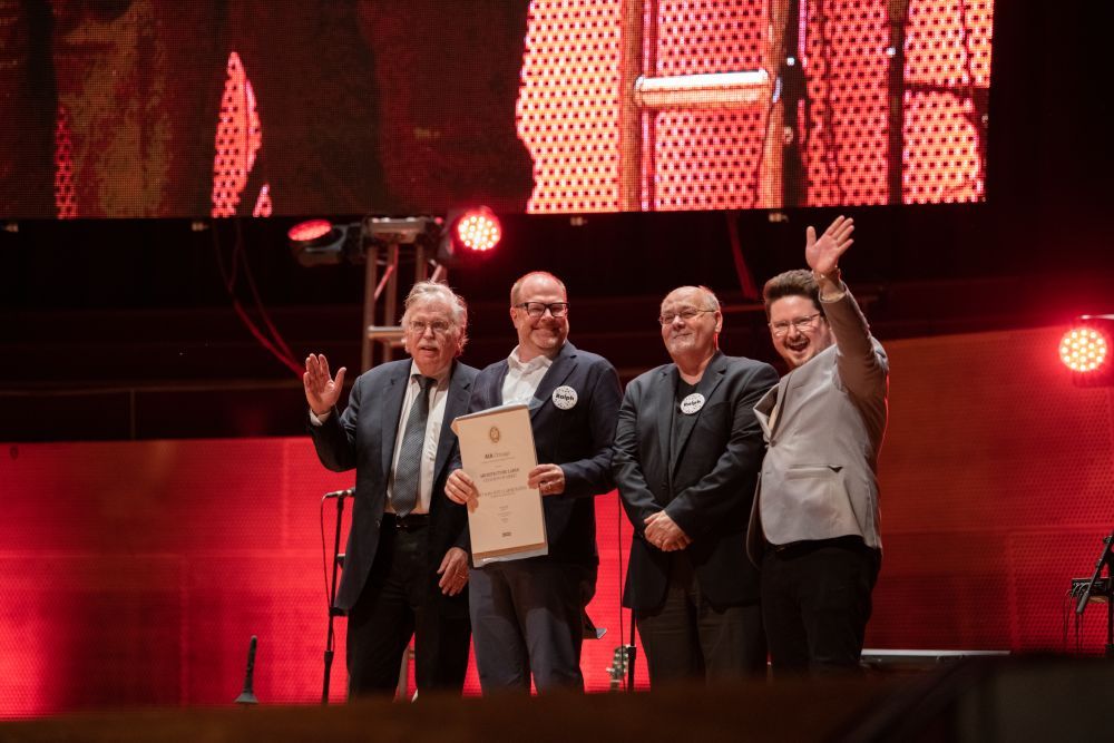A group of four men on stage posing, smiling, and waving as they receive an award.