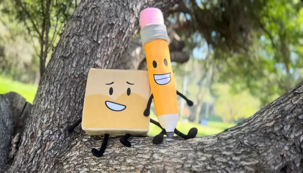 A pencil and notepad with smiling faces sit on a tree branch. 
