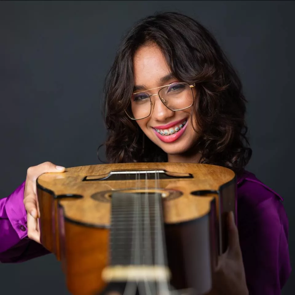 A young girl smiling and holding a cuatro guitar.