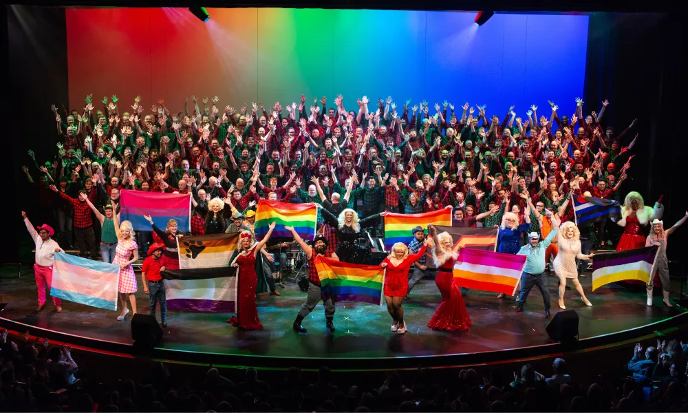 Chicago Gay Men's Chorus on stage holding up different LGBTQIA+ flags.