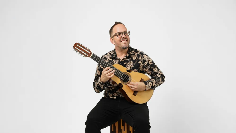 A man smiling while holding a Cuatro guitar. 