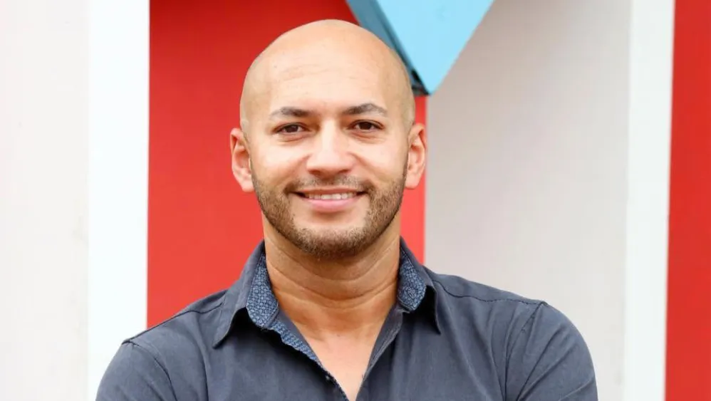 A man smiling in front of the Puerto Rican flag.