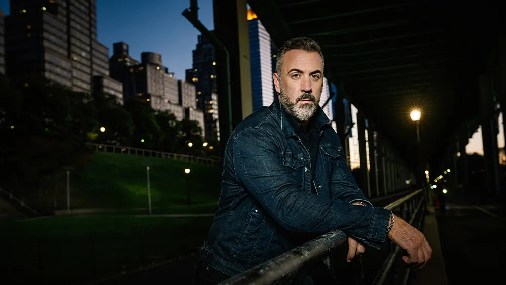 A man posing near a bridge in the late evening. 
