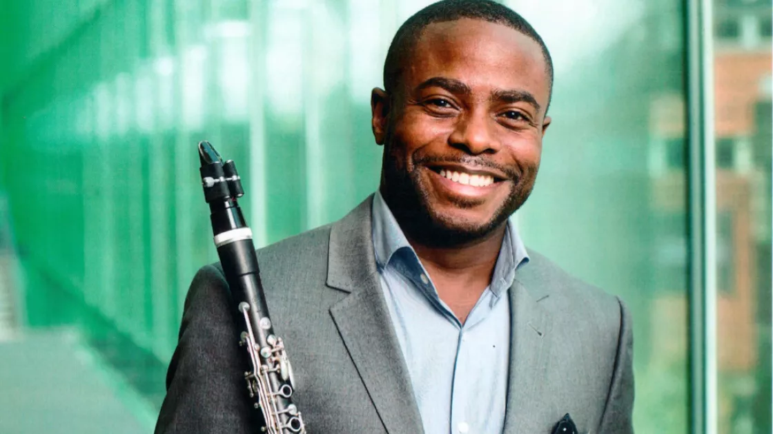 Head shot of artist Anthony McGill, holding his flute and smiling
