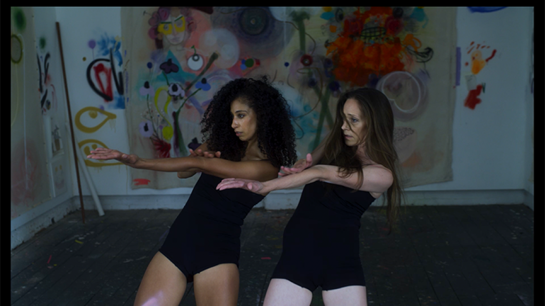 Two dancers extending their arms to their right side with splattered paint as the background.