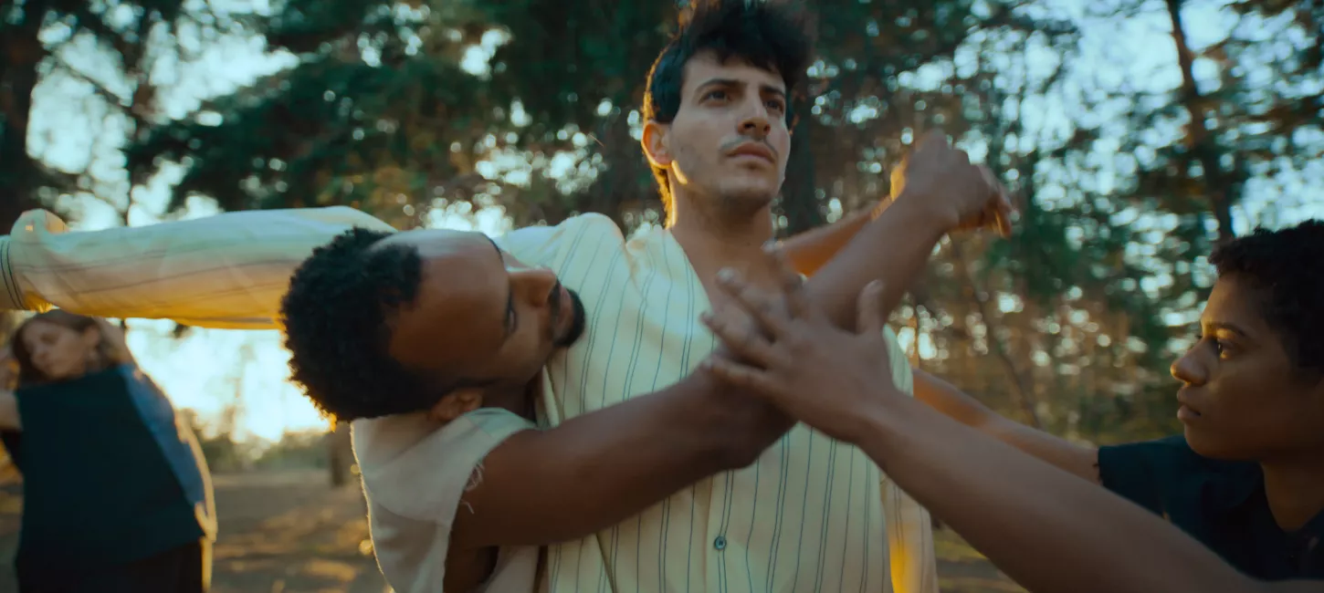 Four dancers in white and grey clothing dance in a wooded setting
