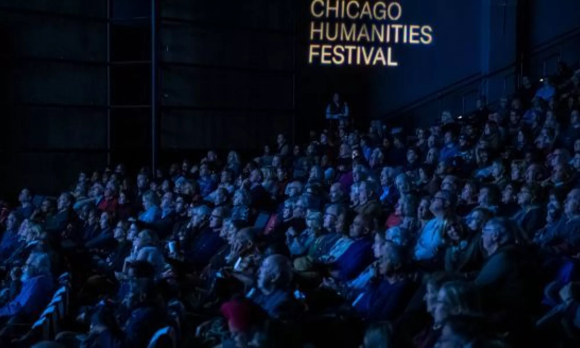 Audience inside the Harris Theater auditorium with Chicago Humanities Festival projected on the walll