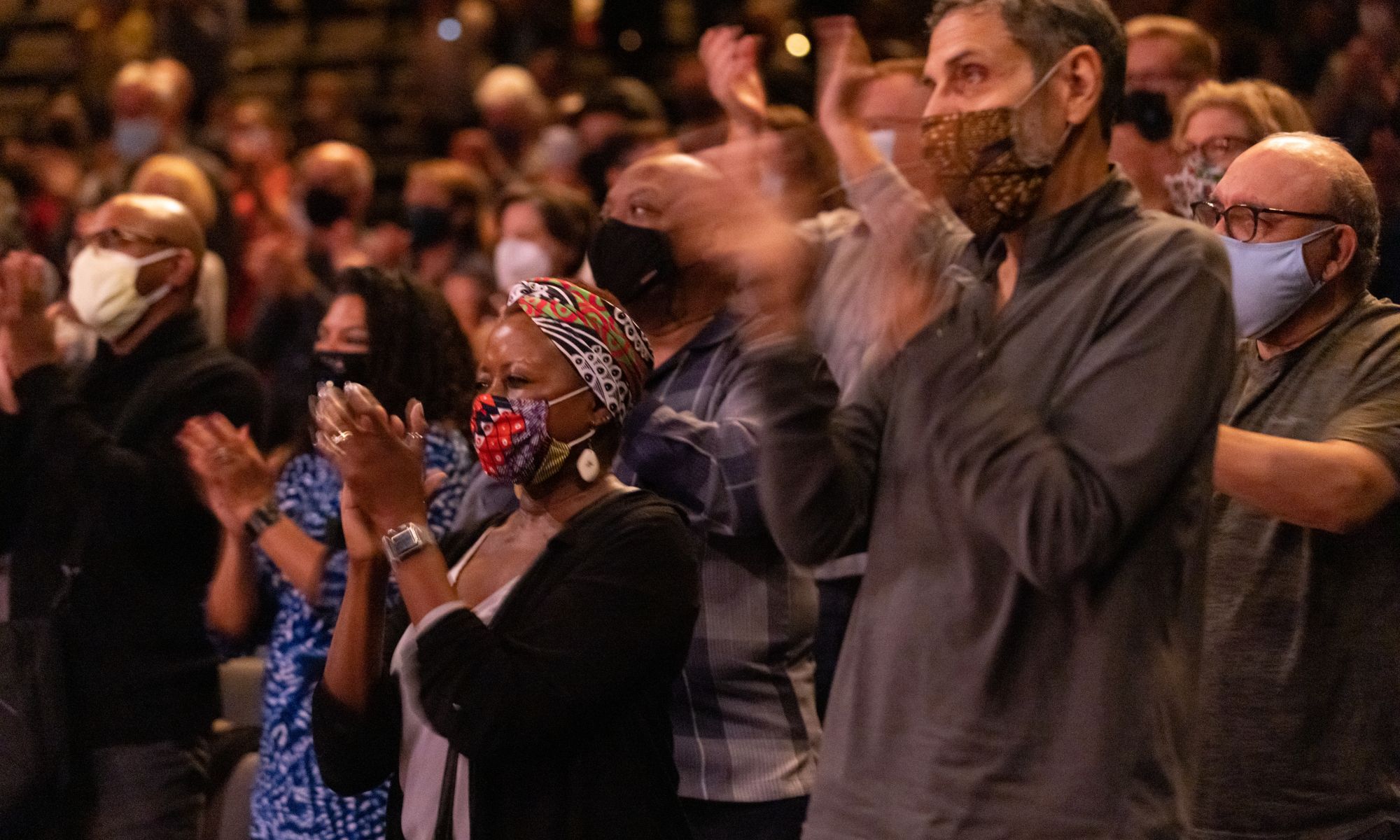 Audience members in a theater applauding, wearing face masks 