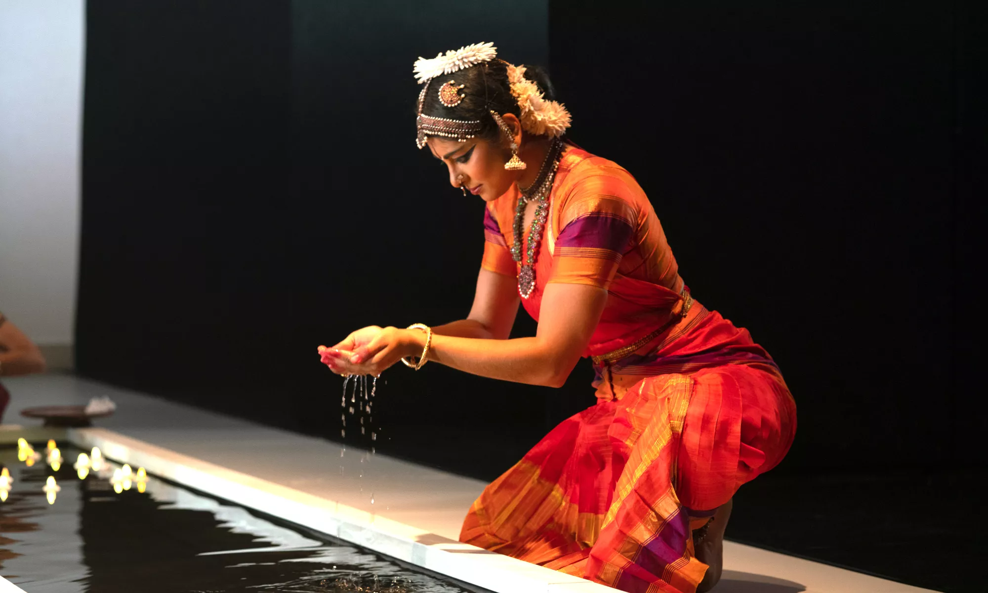 Ragamala Dance Comapany dancer kneeling and holding water in their hands