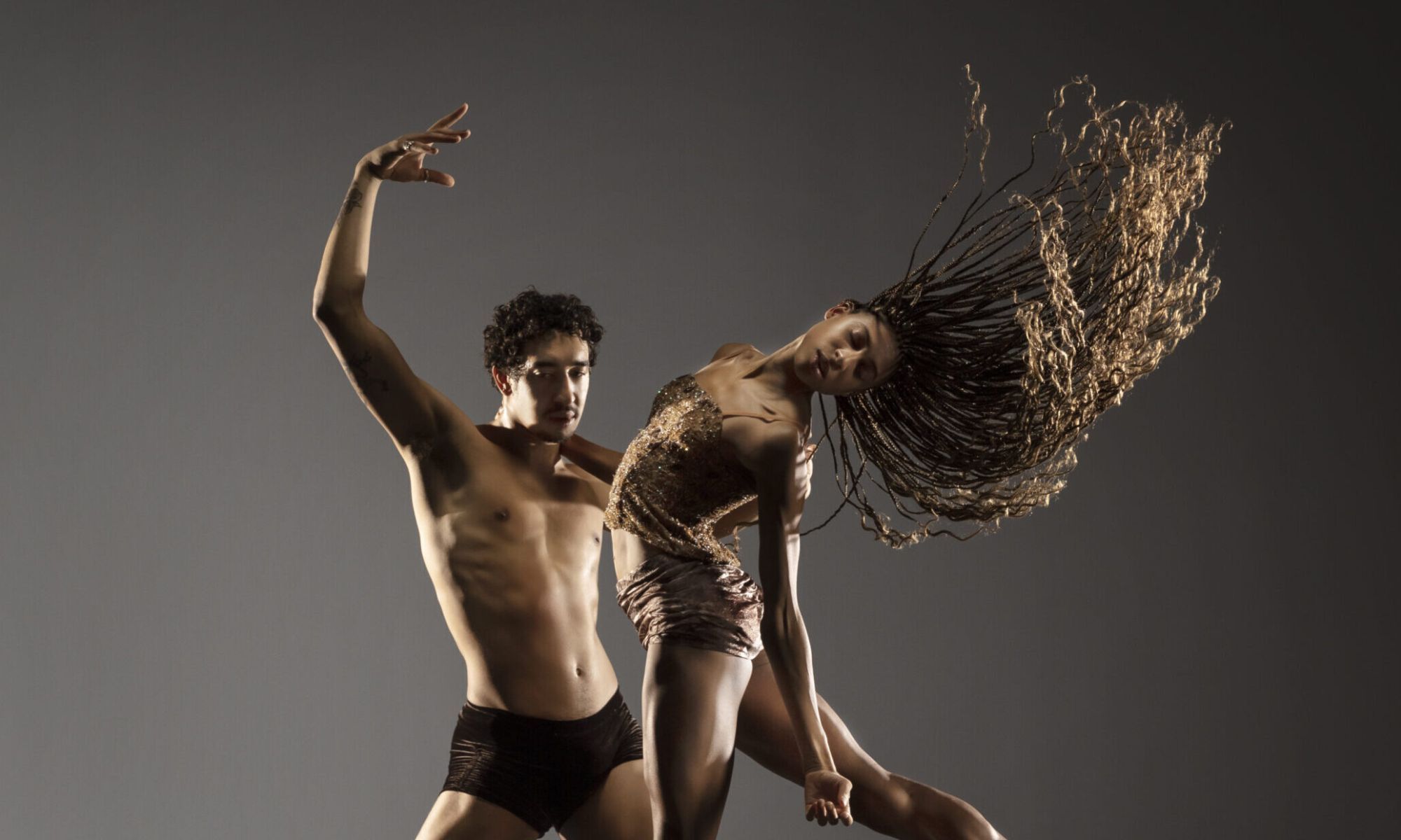 Two dancers pose against a grey backdrop