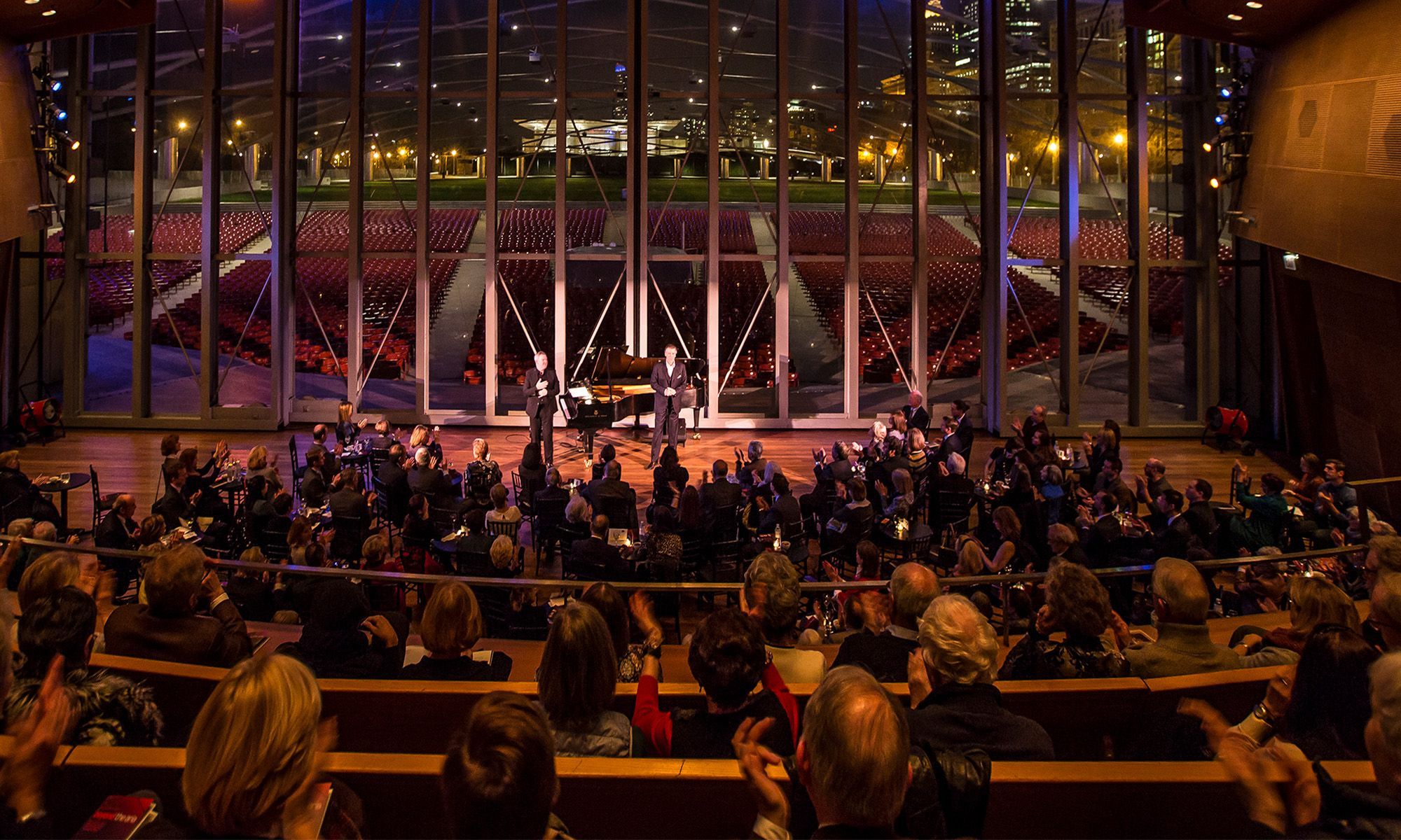 Arial view of an audience looking at the stage where the glass wall behind the performers displays the Chicago skyline at night