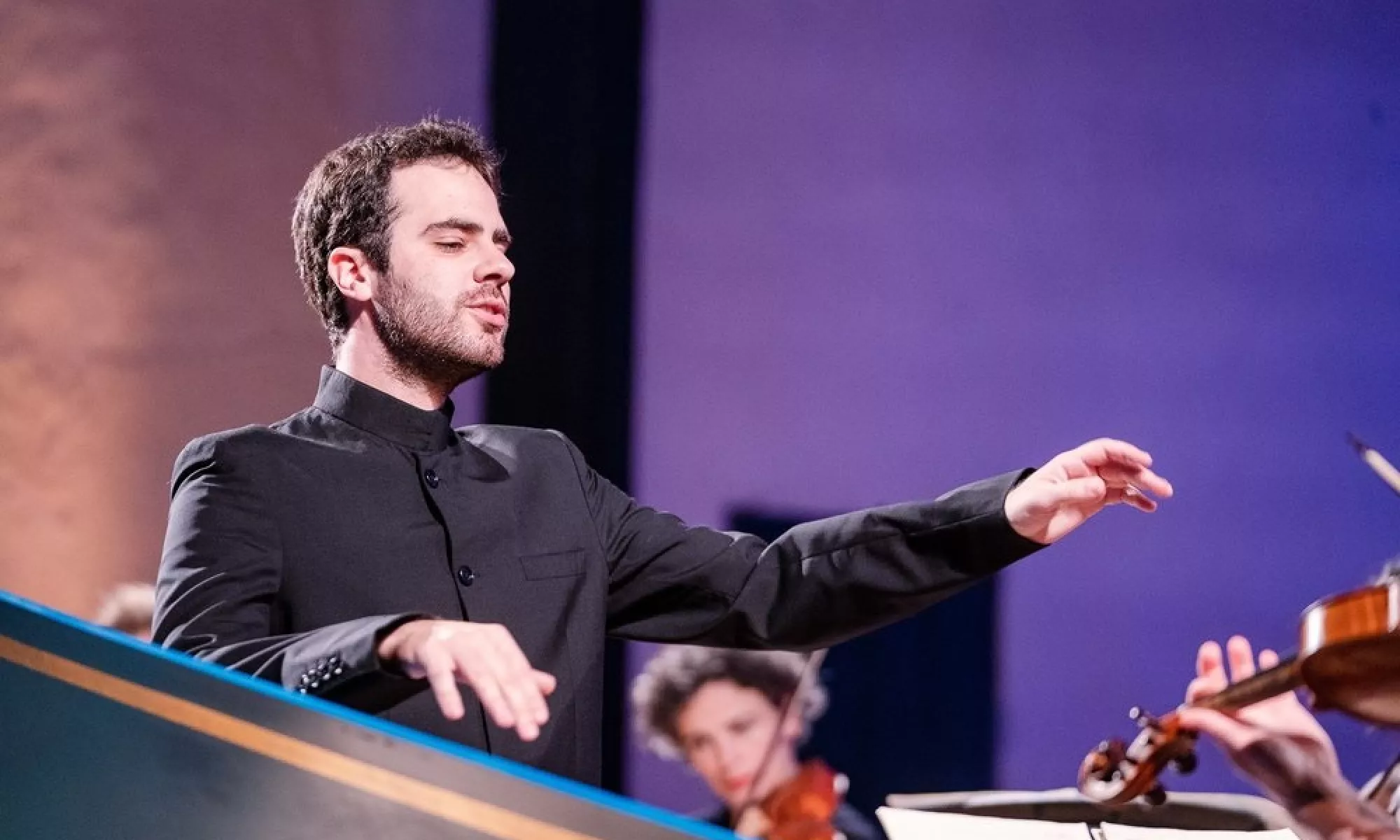 Dinis Sousa lifts his arms as he is in the middle of conducting. His eyes are closed.