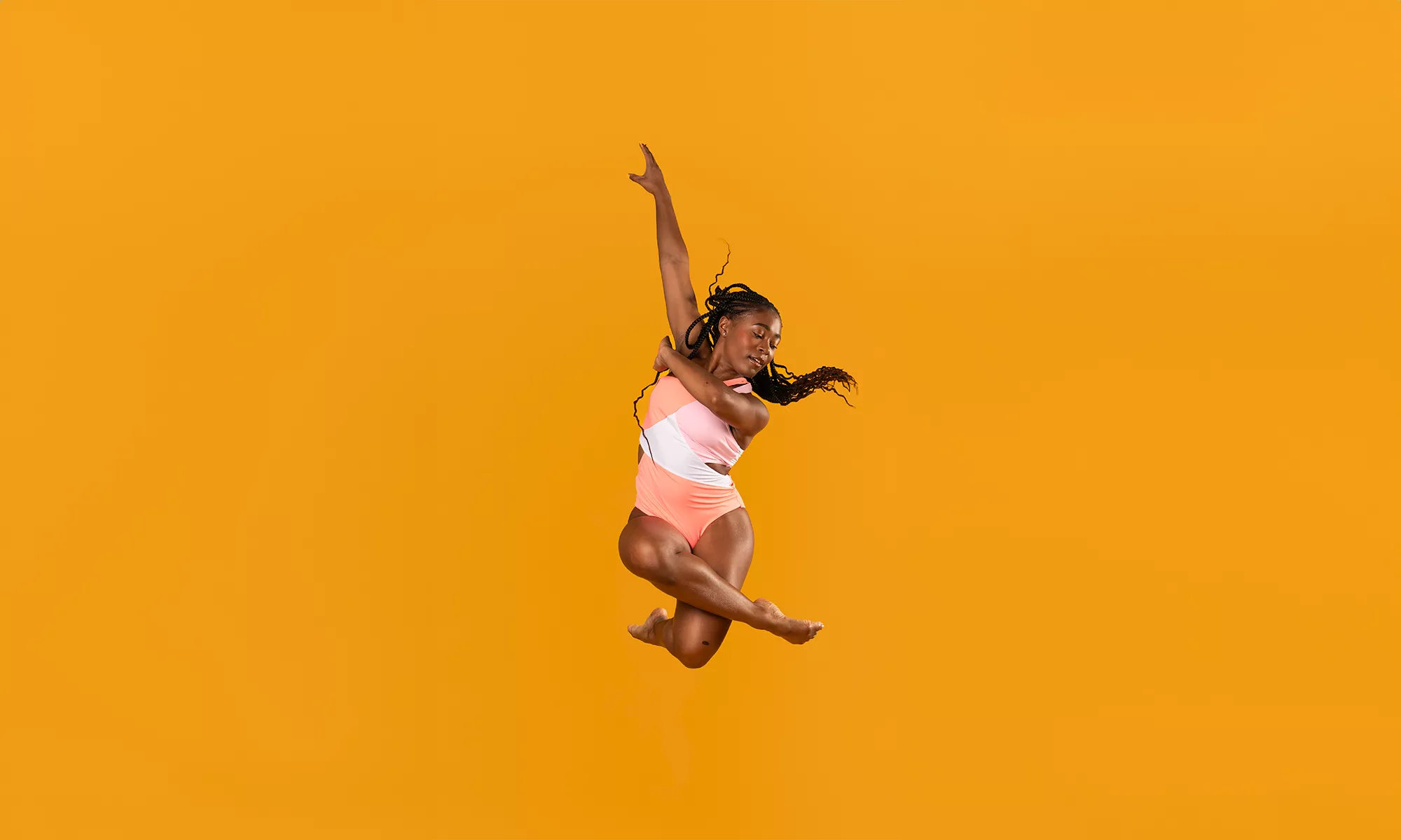 A dancer is mid-air posing with her arms extended and legs crossed.