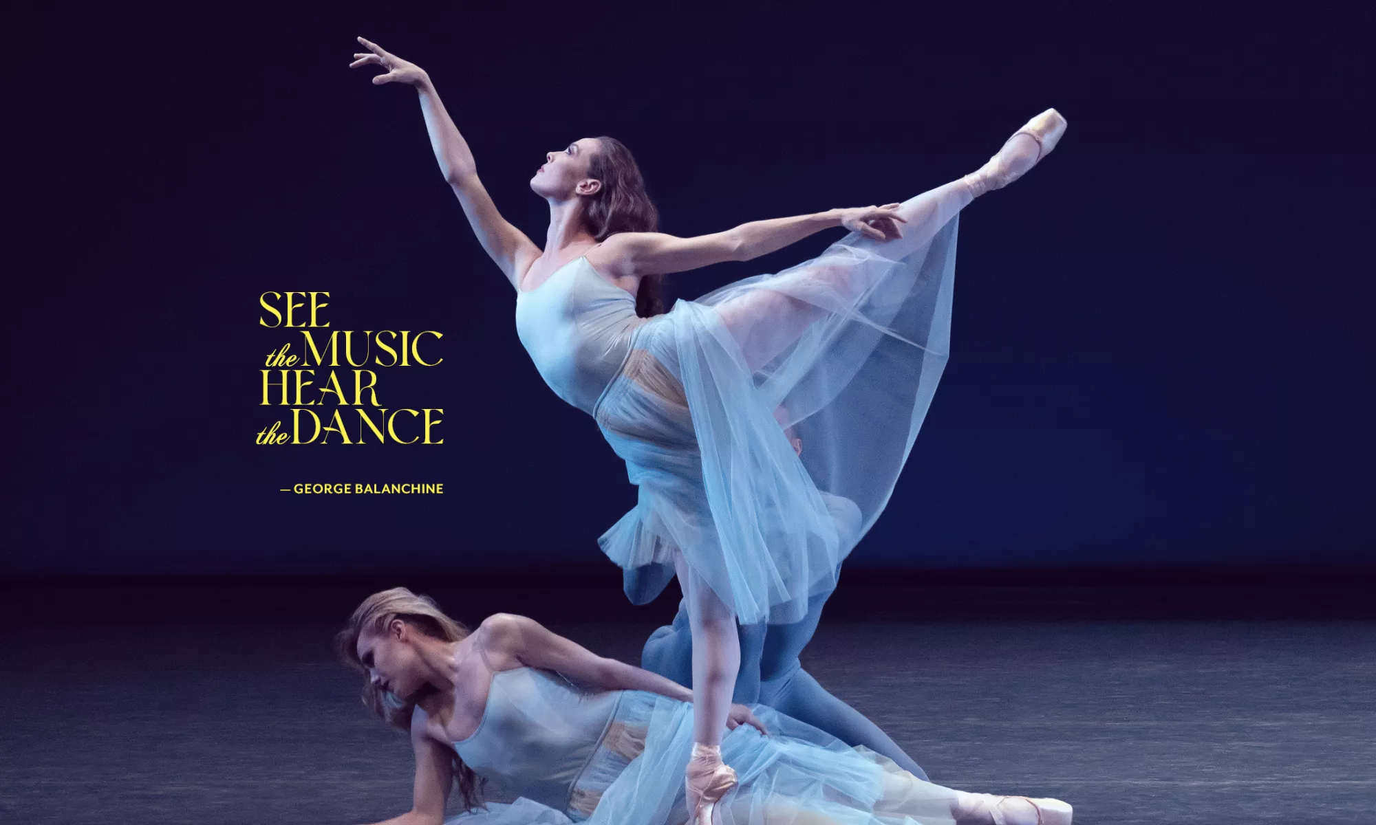 Two dancers on stage with baby blue dresses. One is lying on the floor while the other is in an arabesque position. A third dancer is hidden in the back.