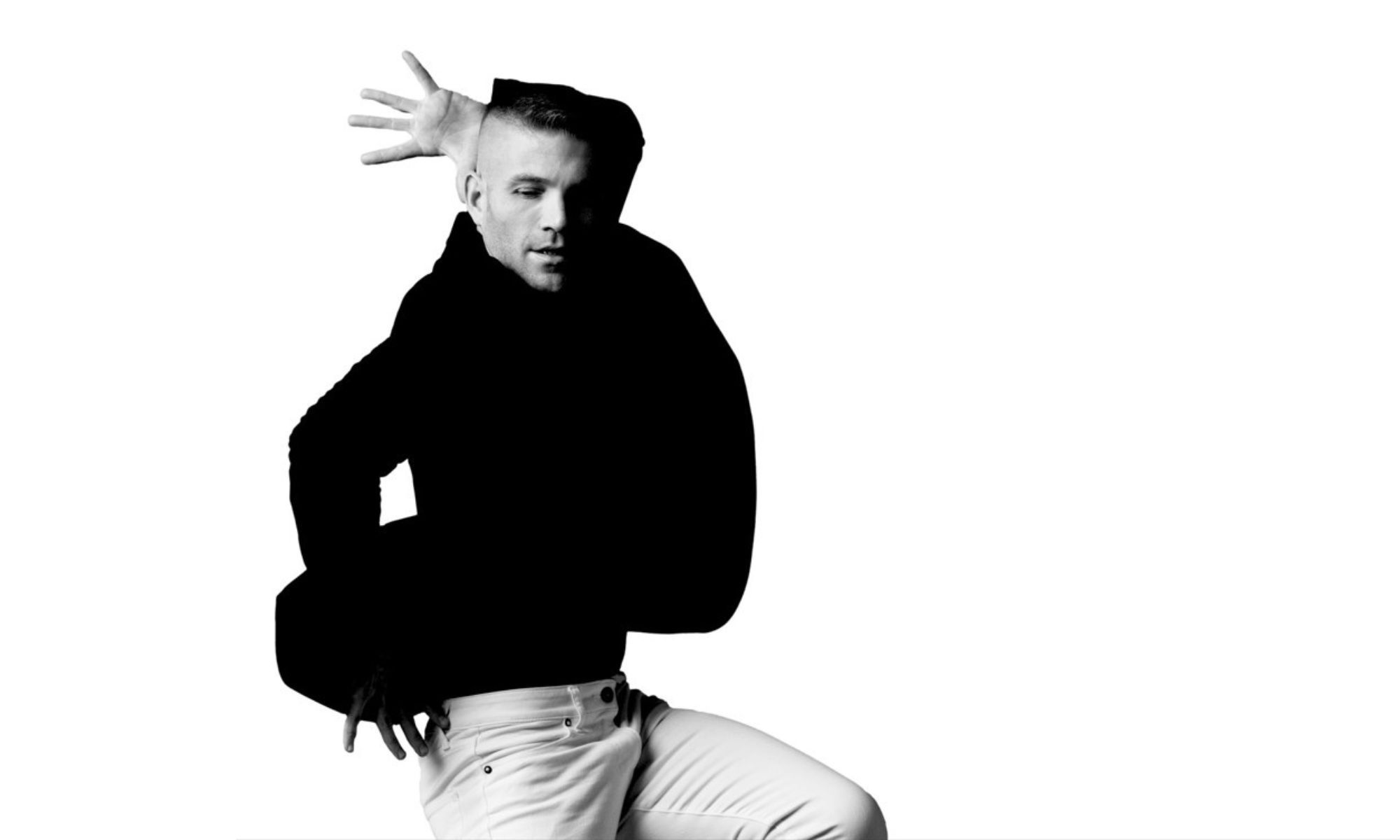 A dancer poses. He wear a black blazer.