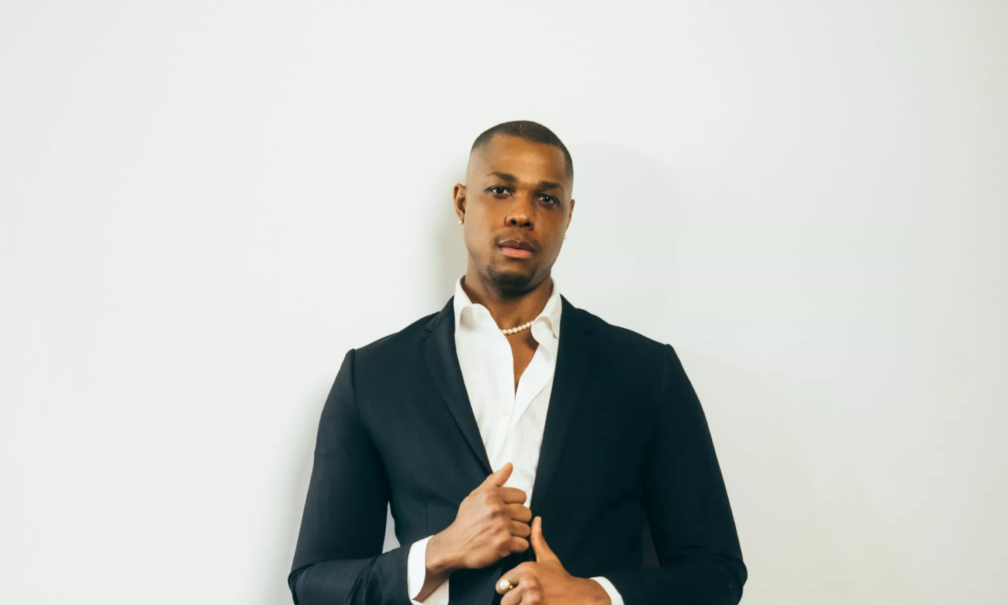 Davóne Tines posing in front of a white wall wearing a suit.