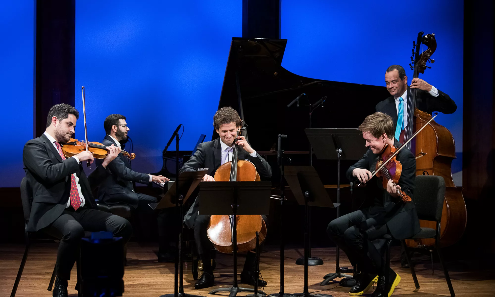 Five musicians playing on stage smiling. 
