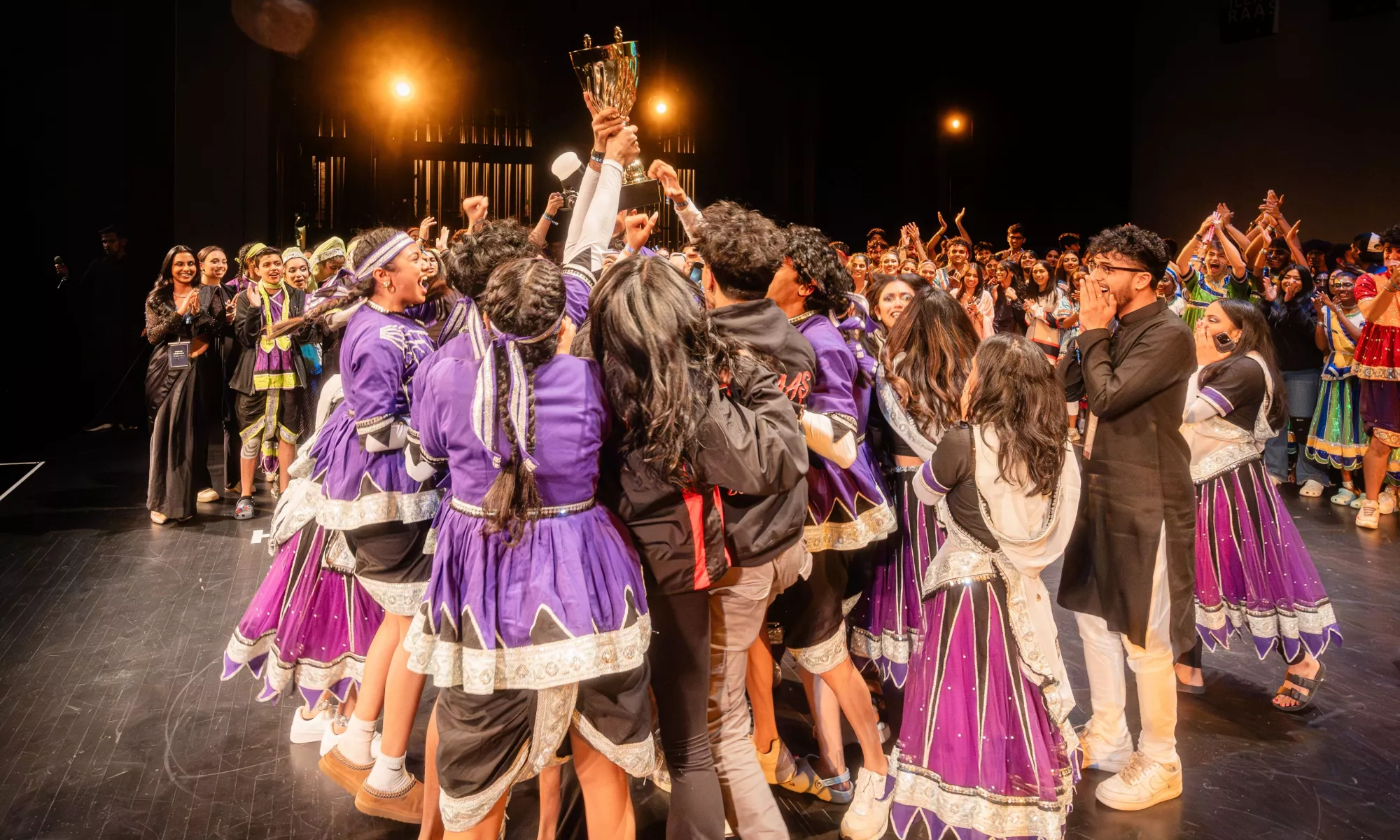 A group of people come together lifting a trophy and celebrating together.