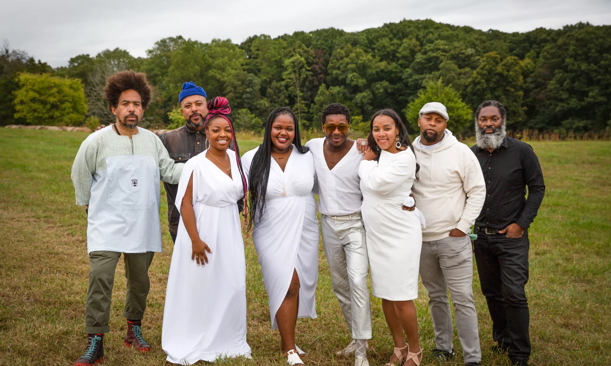 A group of people pose together outside in a park and forest.