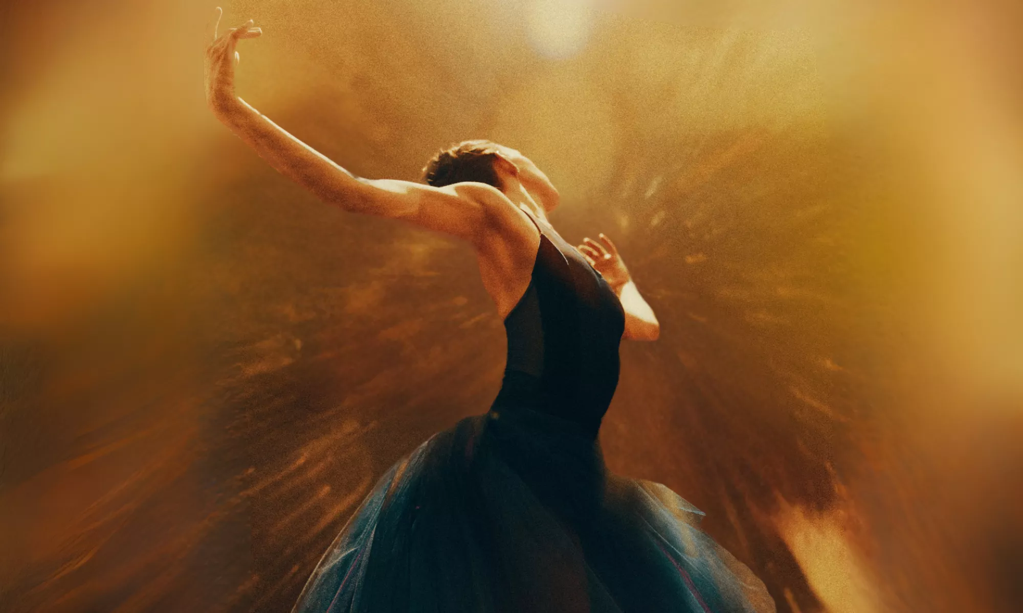 A ballerina looking away with her arms extended upward. A golden light burst and shine in the foreground.