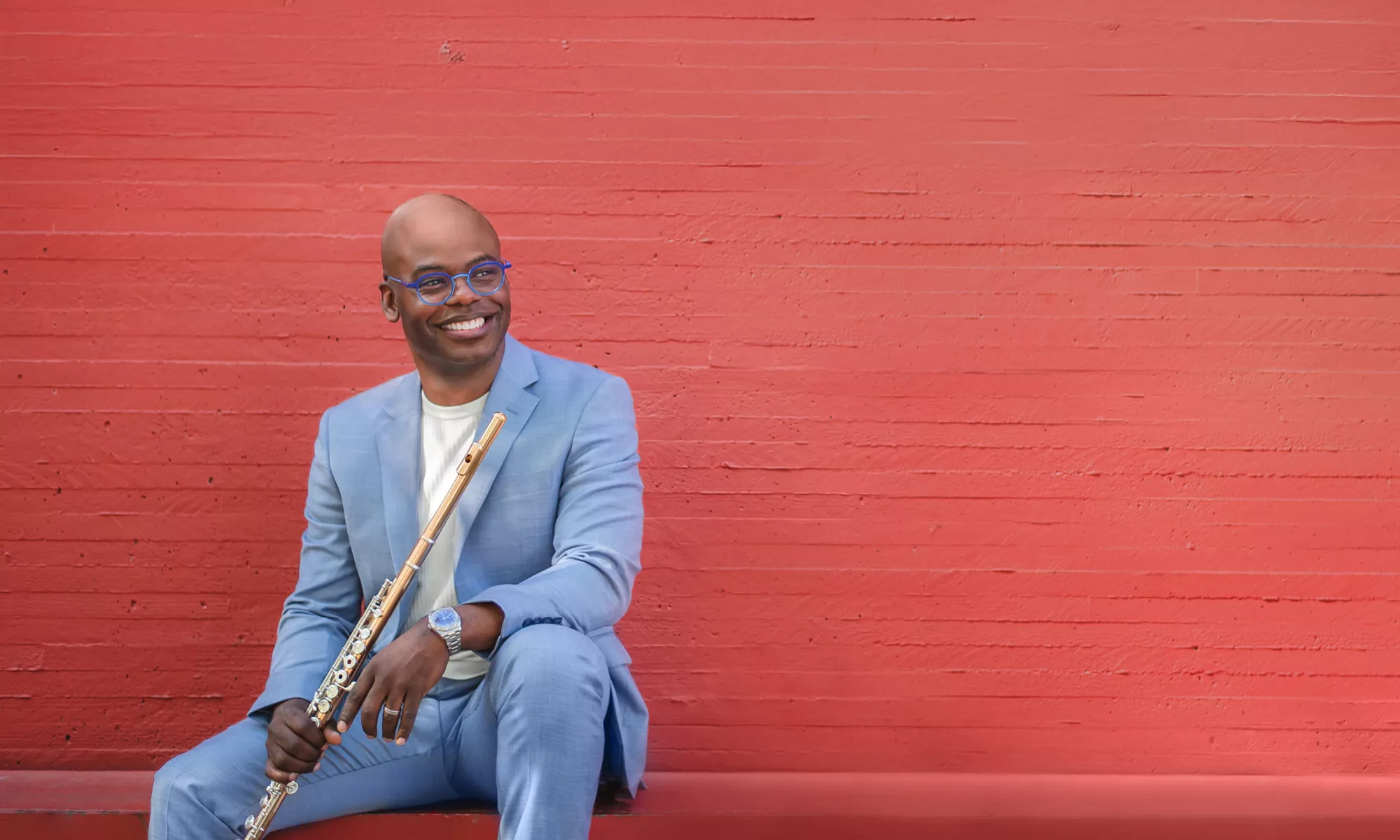 Demarre McGill sits against an orange background holding his flute.