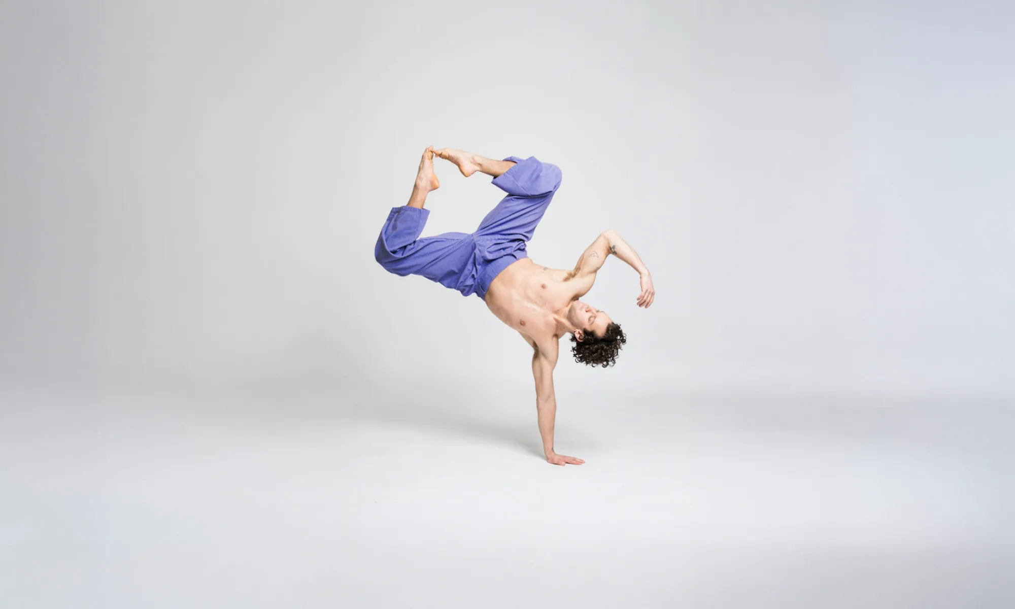 A dancer on stands on one arm with his legs come together. 