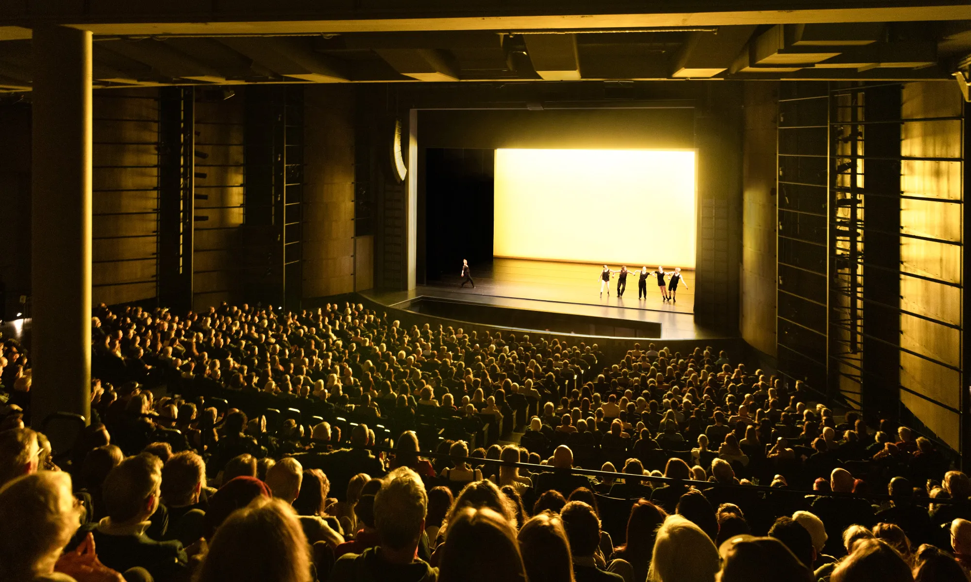 A full Harris Theater auditorium. The audience watches a dance performance where a yellow light is emitted.