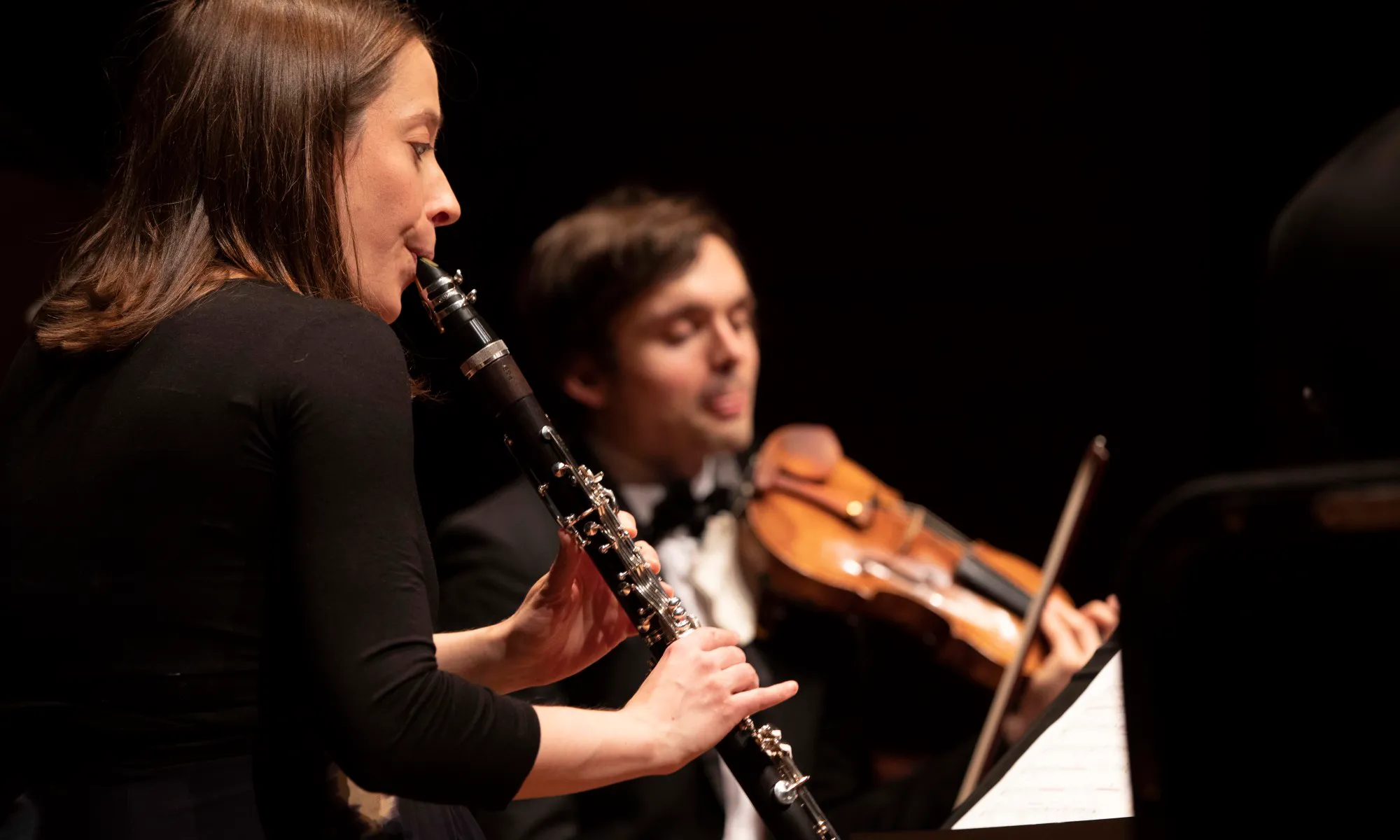 A woman playing the clarinet while a man plays the violin