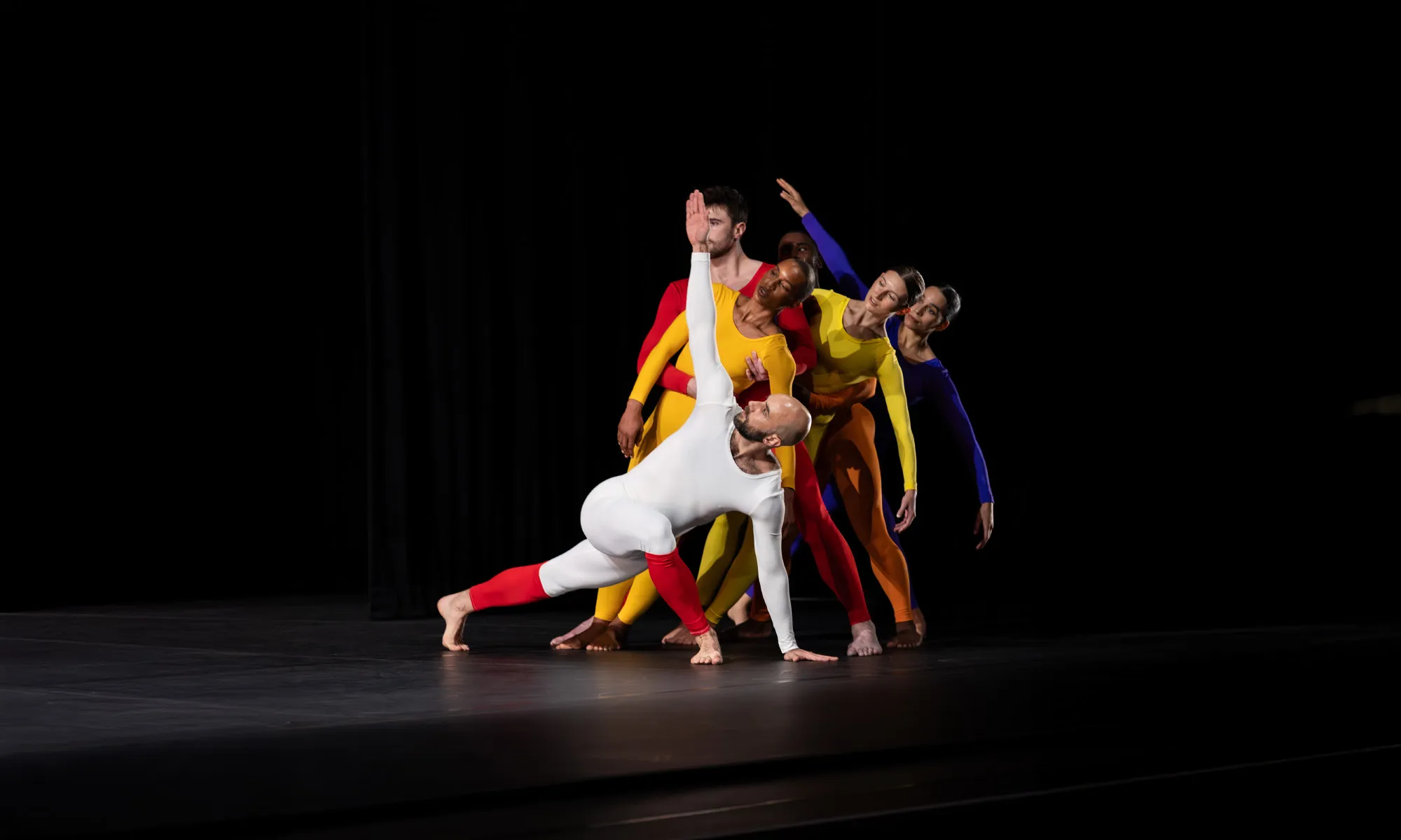 Dancers in different color bodysuits join together.