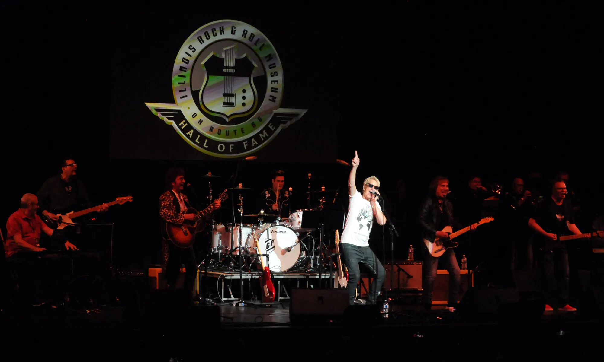 REO Speedwagon’s Kevin Cronin performs onstage with the band beneath the illuminated Illinois Rock & Roll Museum Hall of Fame logo during a live set.