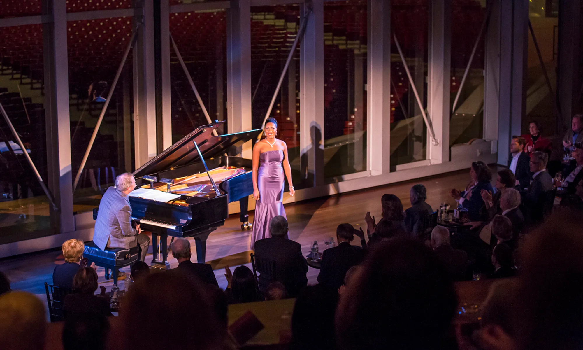 J'Nai Bridges performing in front of an audience while Craig Terry plays the piano.