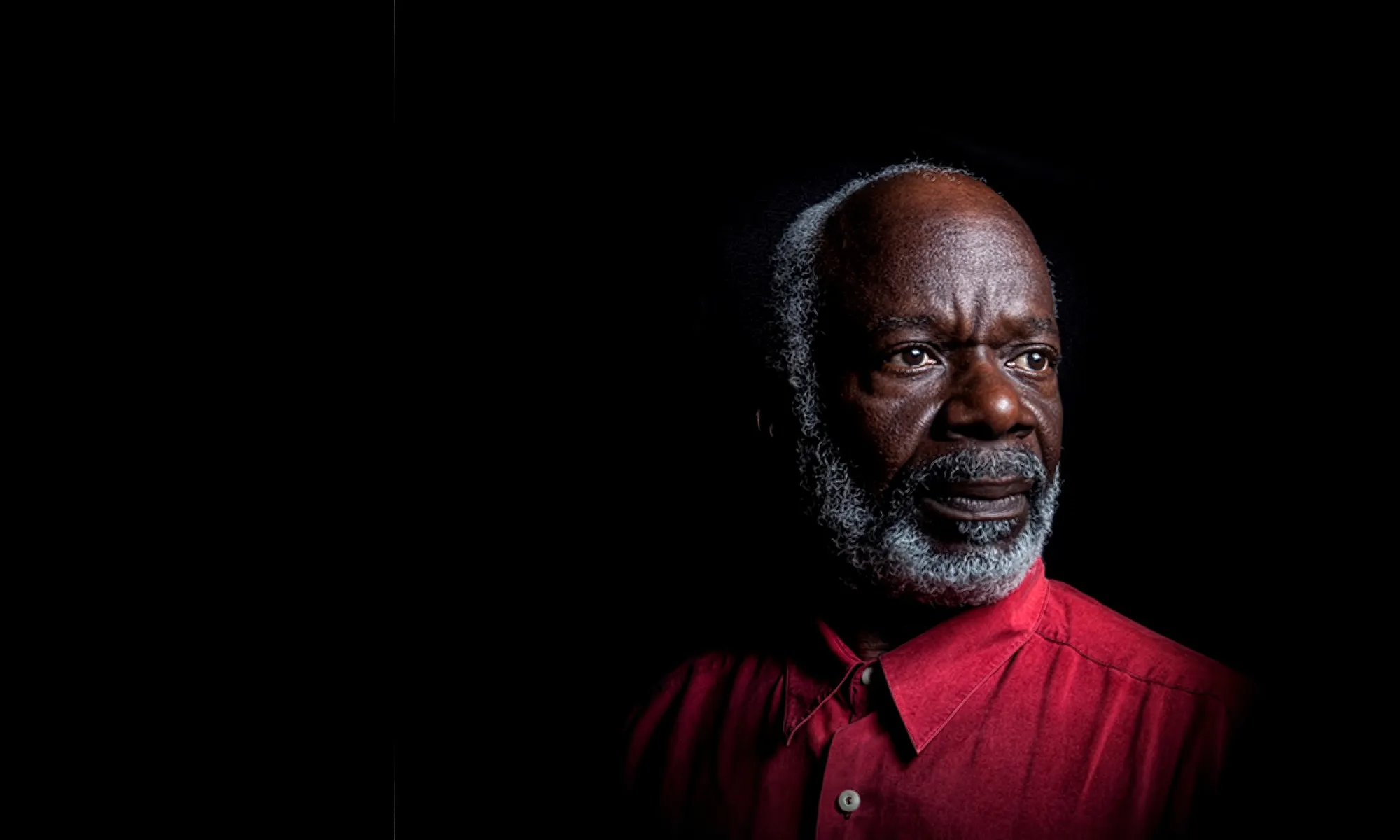 Actor Joseph Marcell in a red shirt on a black background
