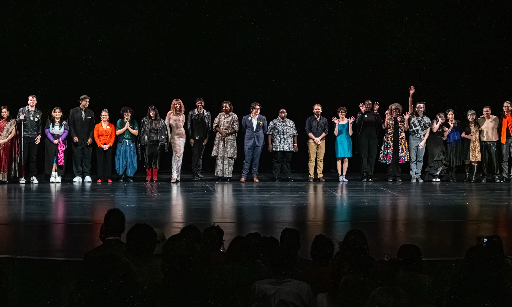 2025 3Arts Awardees standing in a curtain call line on the Harris Theater stage, waving and smiling at the audience.