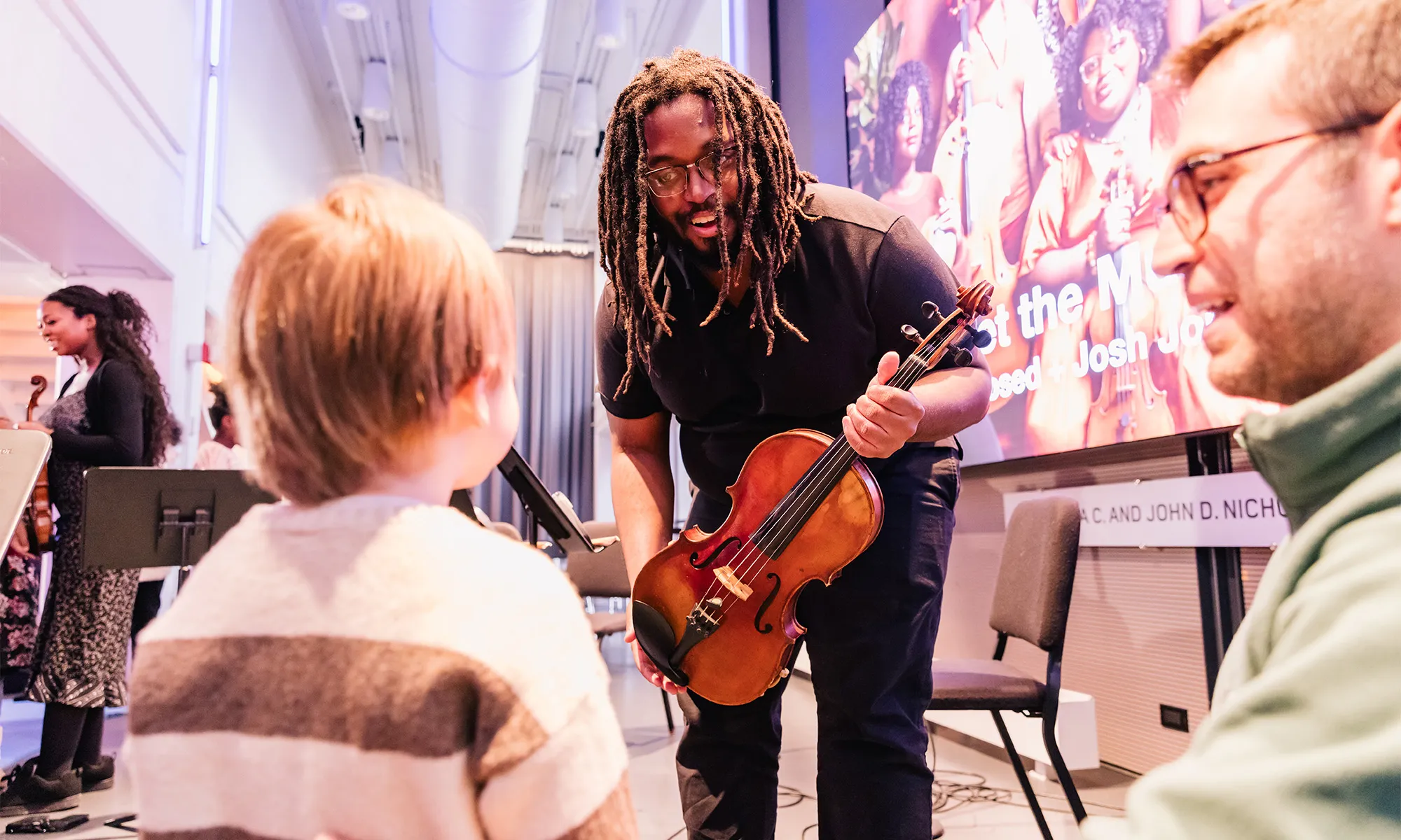 A young boy and his dad interacting with a violinist. 
