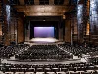 Image of an empty auditorium. The image is centered with a purple gradient screen on stage.
