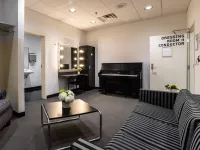 Image of Dressing Room 1 filled with a piano, a vanity mirror setup, a couch, accent chair, and small table fill the room. A sink indicating a bathroom is shown.