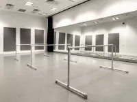Image of an empty rehearsal room filled with wall mirrors and three bars for dancers. 