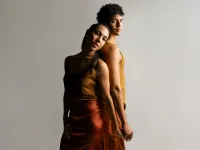 A man and woman stand back-to-back while holding hands. 