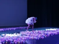 A performer on stage bending and looking down. There are flowers all over the floor.