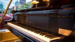 Close-up image of a black grand piano, with an outdoor pavilion and Chicago skyline in the background