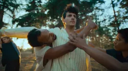 Four dancers in white and grey clothing dance in a wooded setting