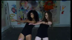 Two dancers extending their arms to their right side with splattered paint as the background.