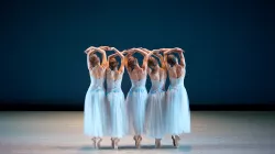 Five dancers wearing light blue tulle dresses raising their arms up