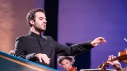 Dinis Sousa lifts his arms as he is in the middle of conducting. His eyes are closed.