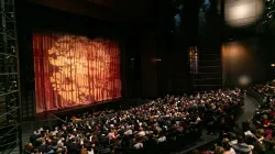 Image of the Harris Theater auditorium filled with people sitting down. 