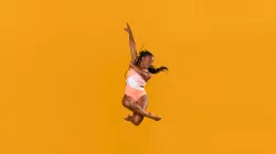 A dancer is mid-air posing with her arms extended and legs crossed. 