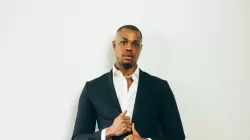 Davóne Tines posing in front of a white wall wearing a suit.